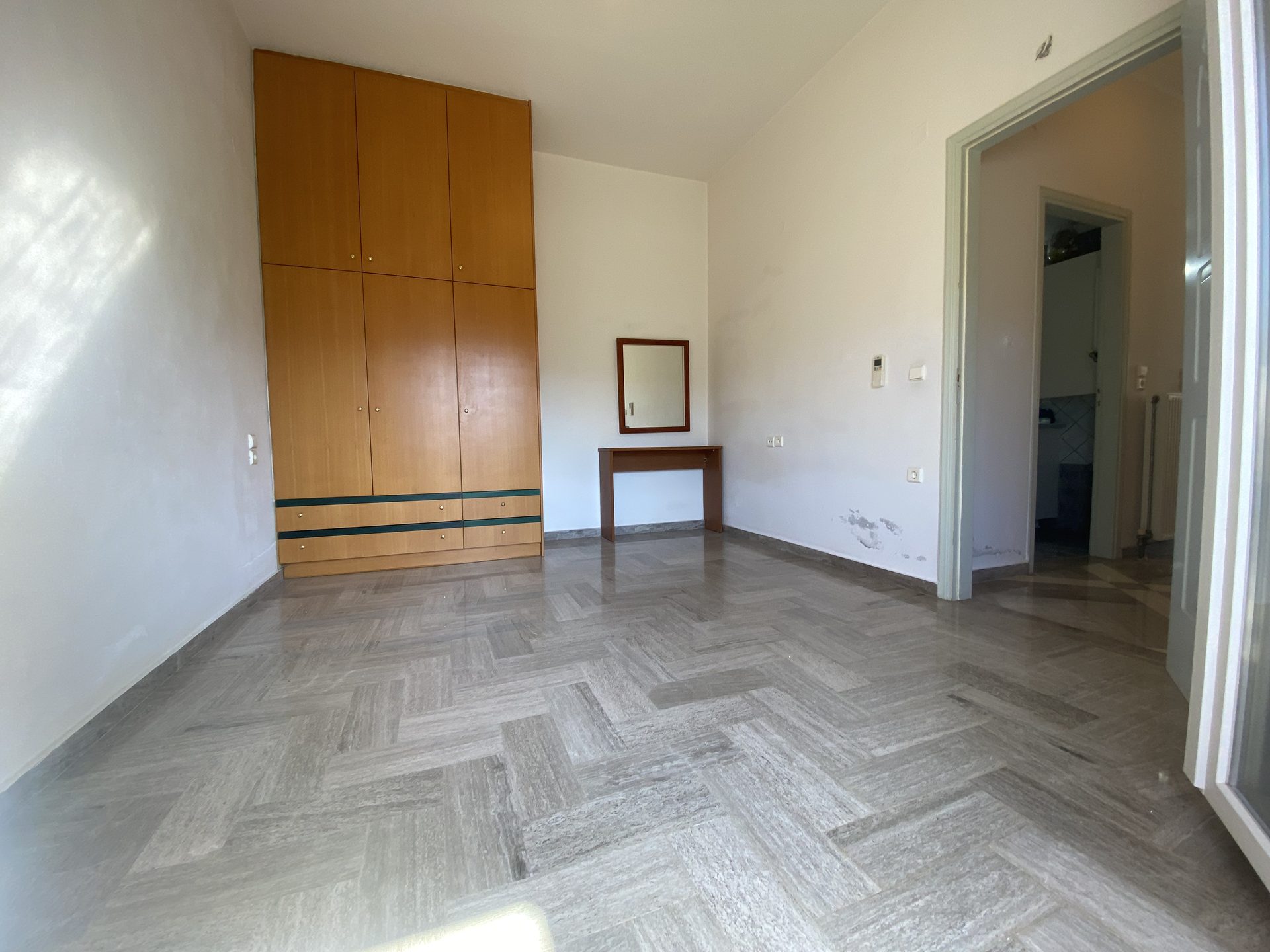 Second bedroom with built-in wardrobes, herringbone floor, and full-height mirror