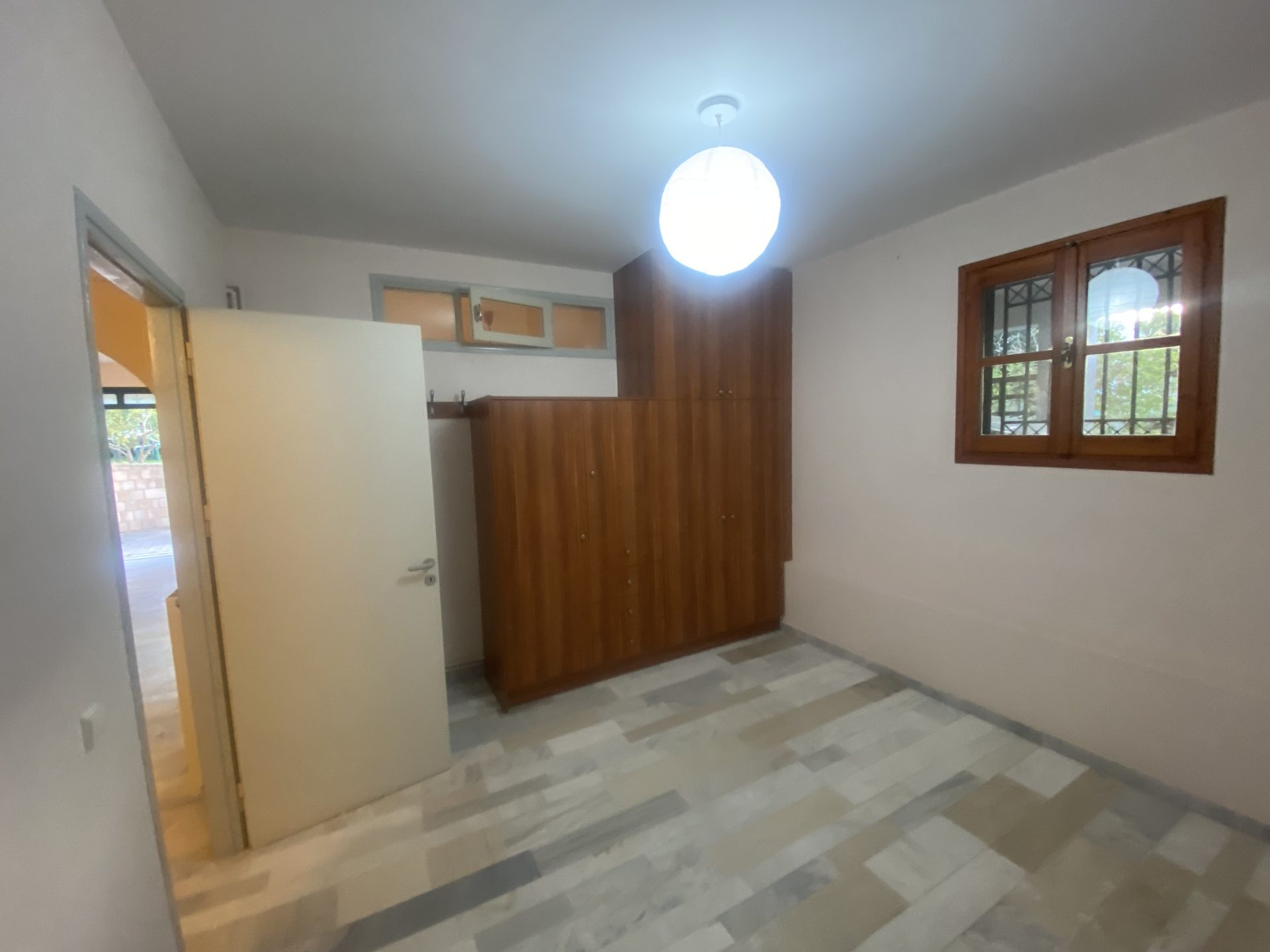 Garden-level bedroom with dark wood wardrobe and grille window