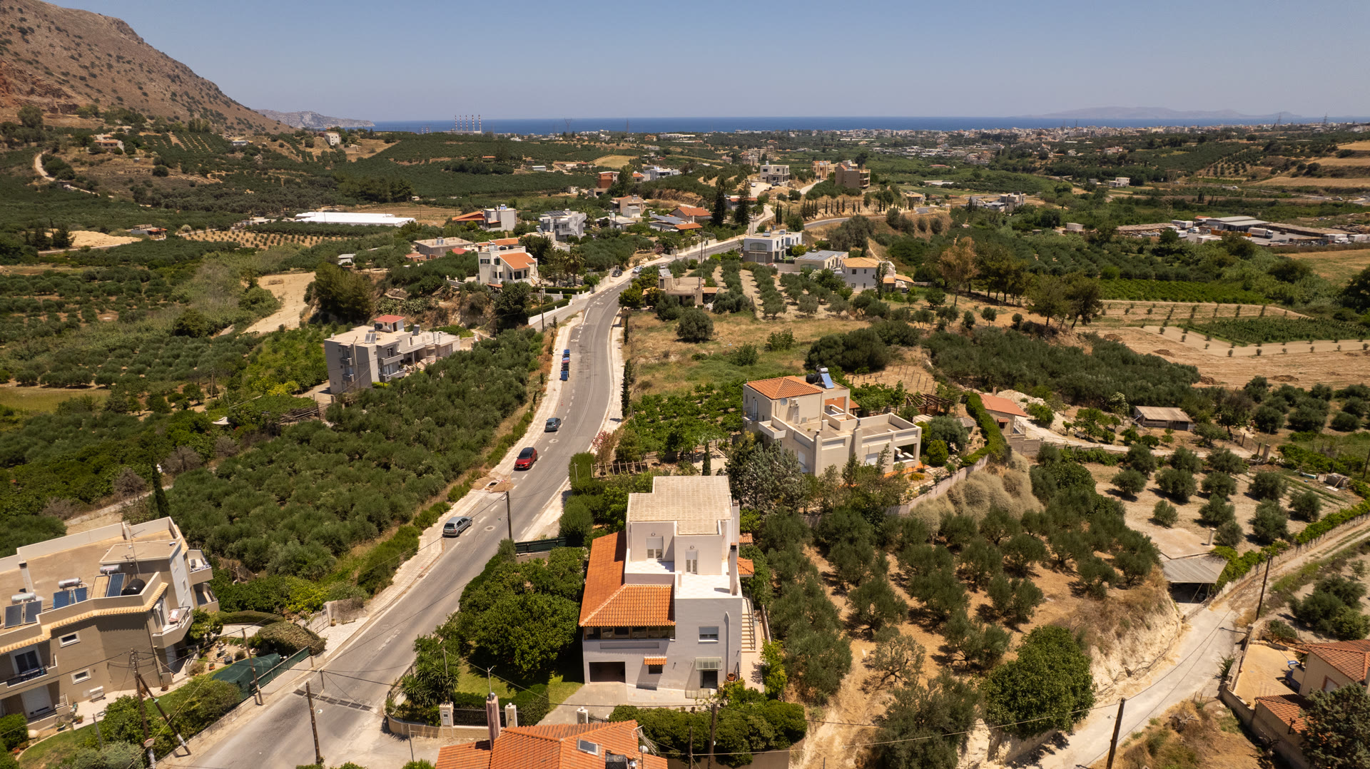 Aerial context showing the house, access road, olive groves, and the coastline beyond
