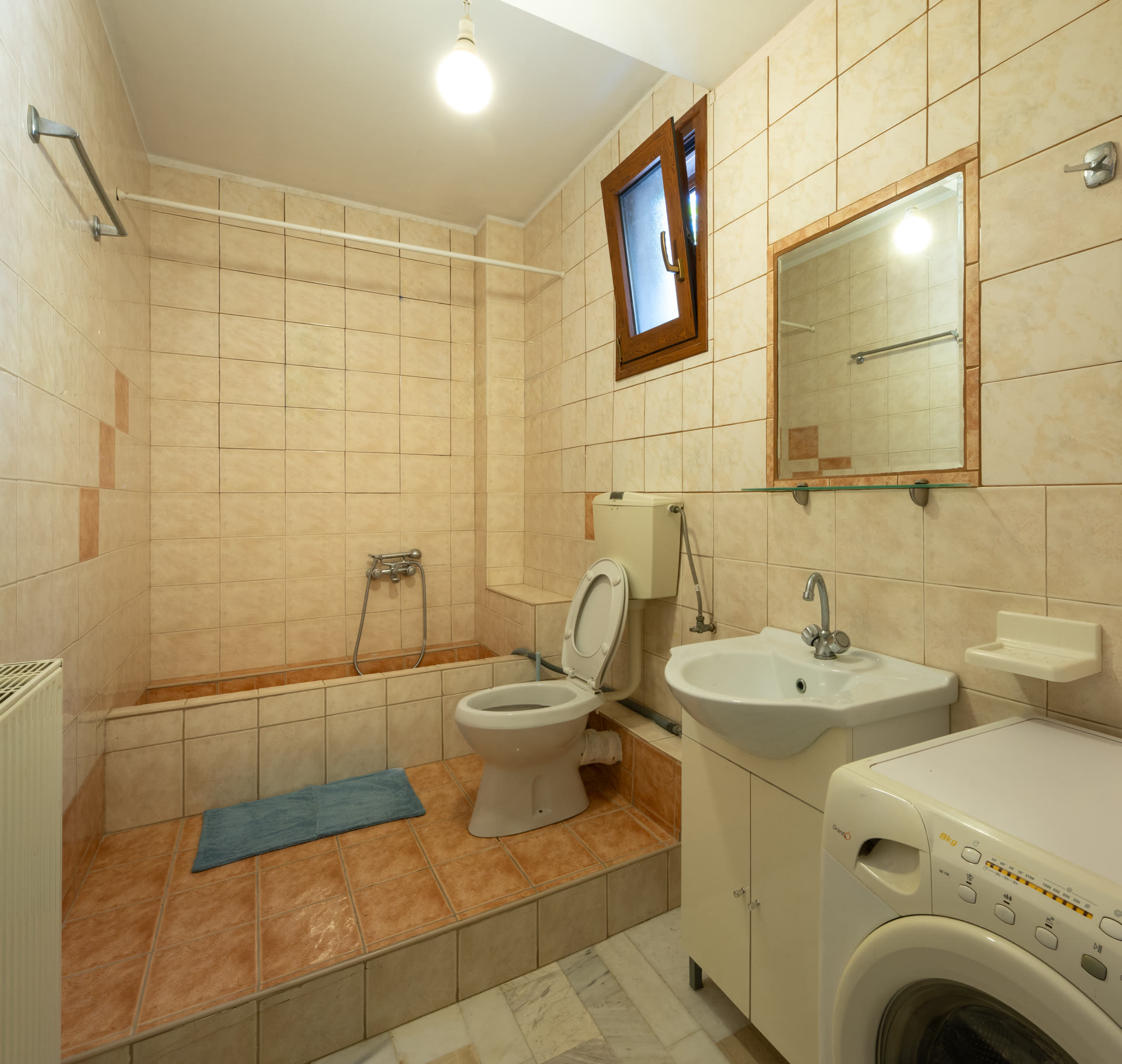 Garden-level bathroom with shower, vanity, washing machine, and small window