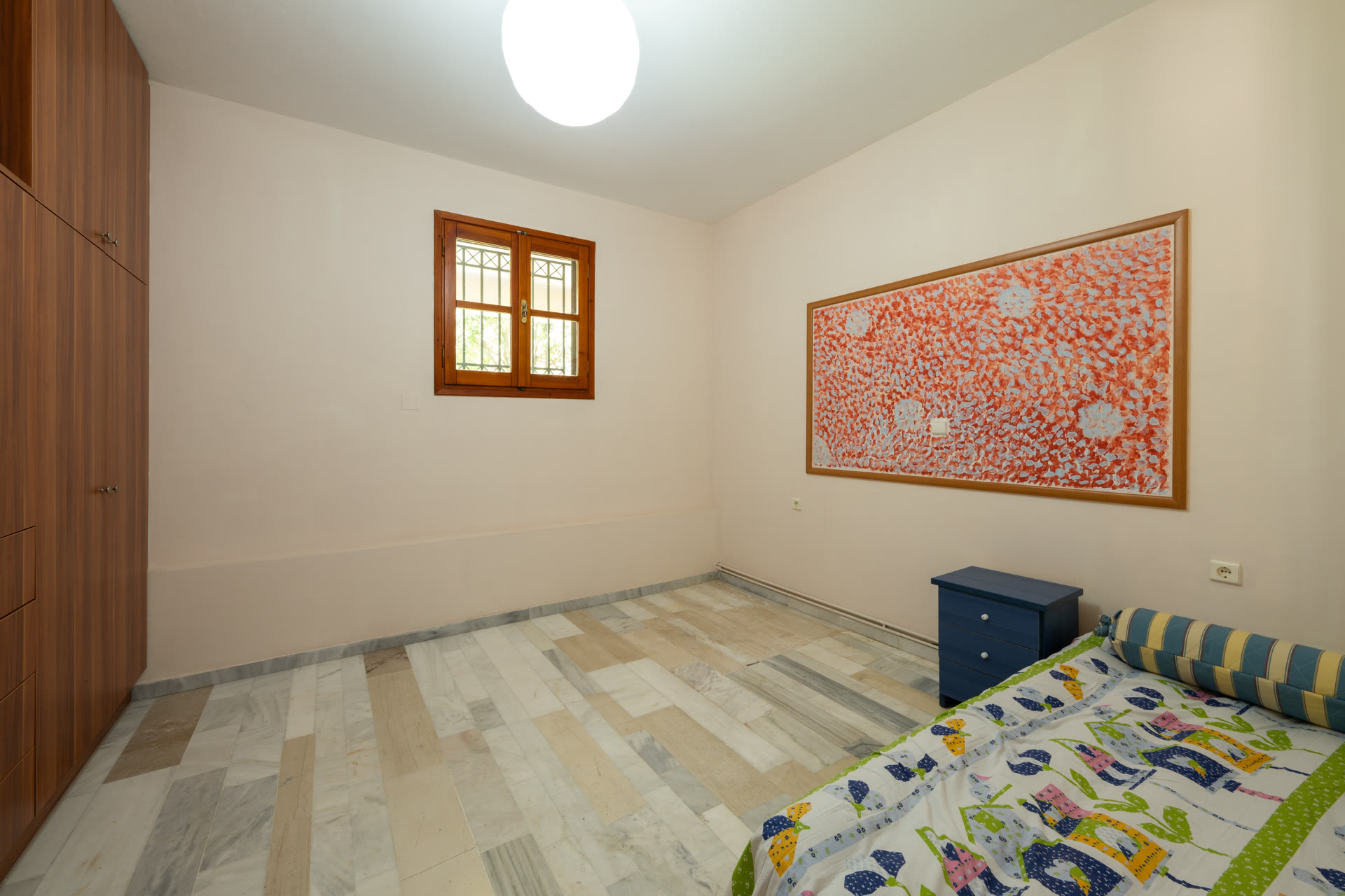 Garden-level bedroom with bed, wardrobe, wall map, and wood-framed window