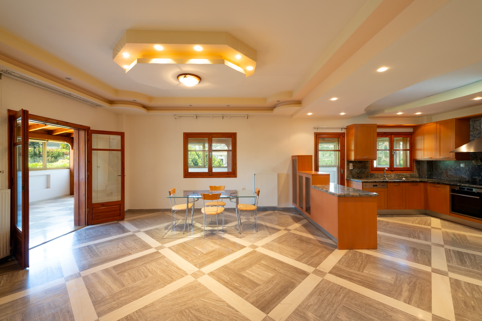 Open living, dining, and kitchen area with marble-pattern floor and wood-framed windows