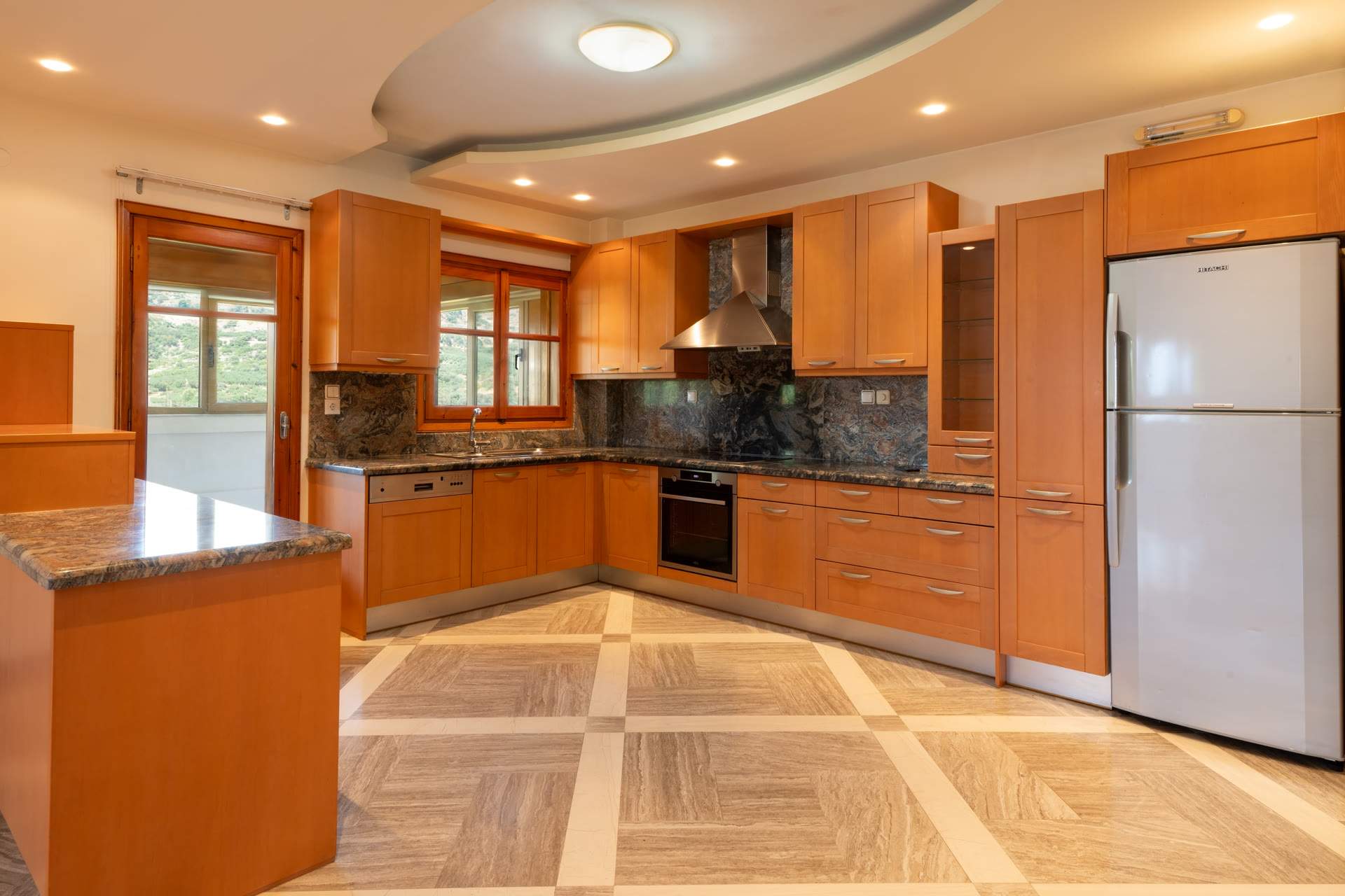 Main kitchen with wood cabinetry, granite worktops, built-in appliances, and window view