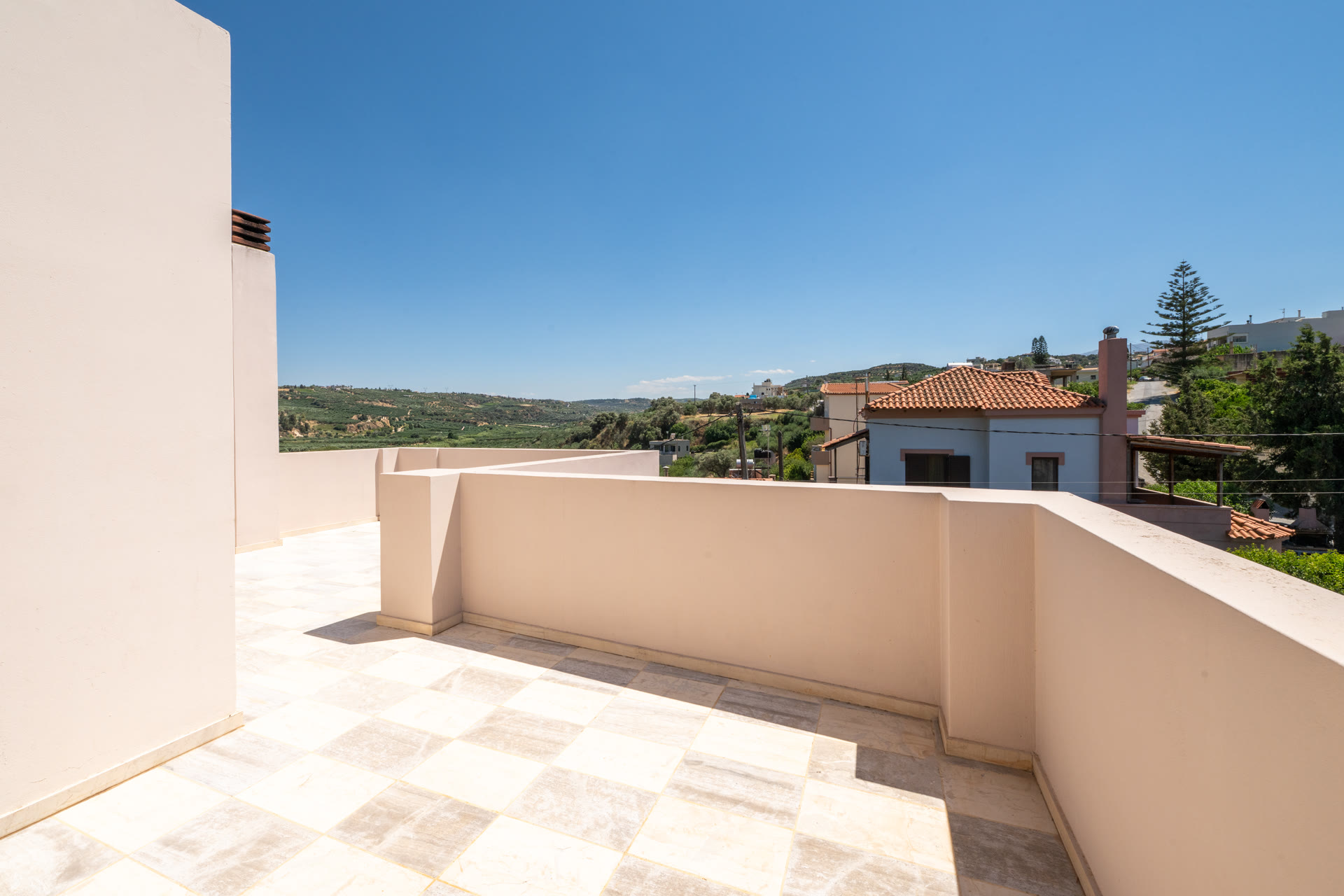 Open roof terrace with village and olive-grove views under a clear blue sky